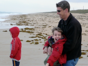 Dad holding Justin on beach by young boy