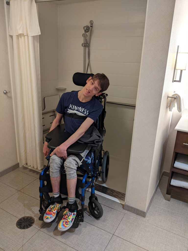 Justin, a young man, sitting in manual wheelchair that's backed into a roll-in shower