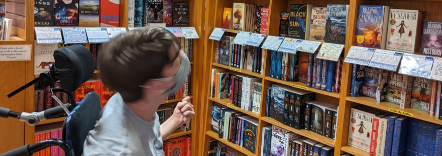 Justin in wheelchair, wearing mask, looking at book store book shelves
