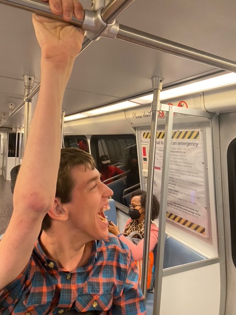 Justin laughing holding onto handrail above him in subway car