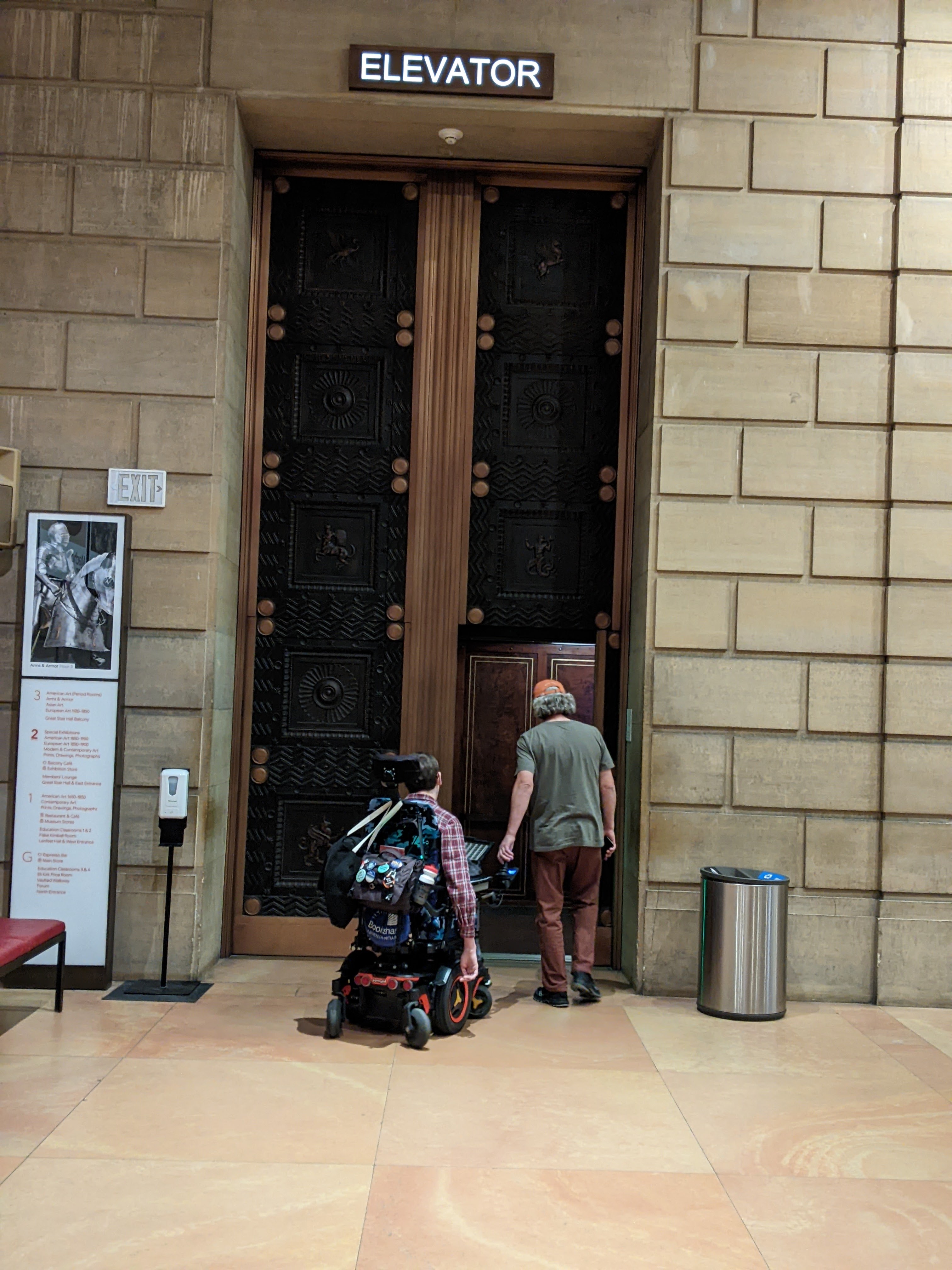 Man in wheelchair and his dad standing next to him entering an elevator with a very tall door