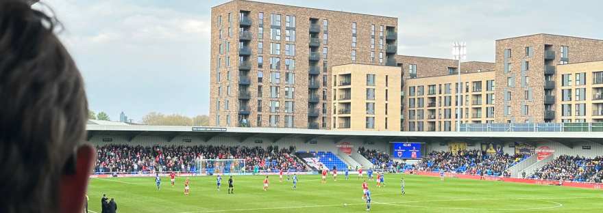 back of Justin's head looking at AFC Wimbledon team playing on pitch, buildings and crowded stadium