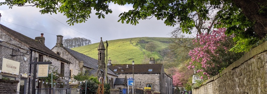 Castleton street with stone buildings, pink flowering trees, green hill, stone wall