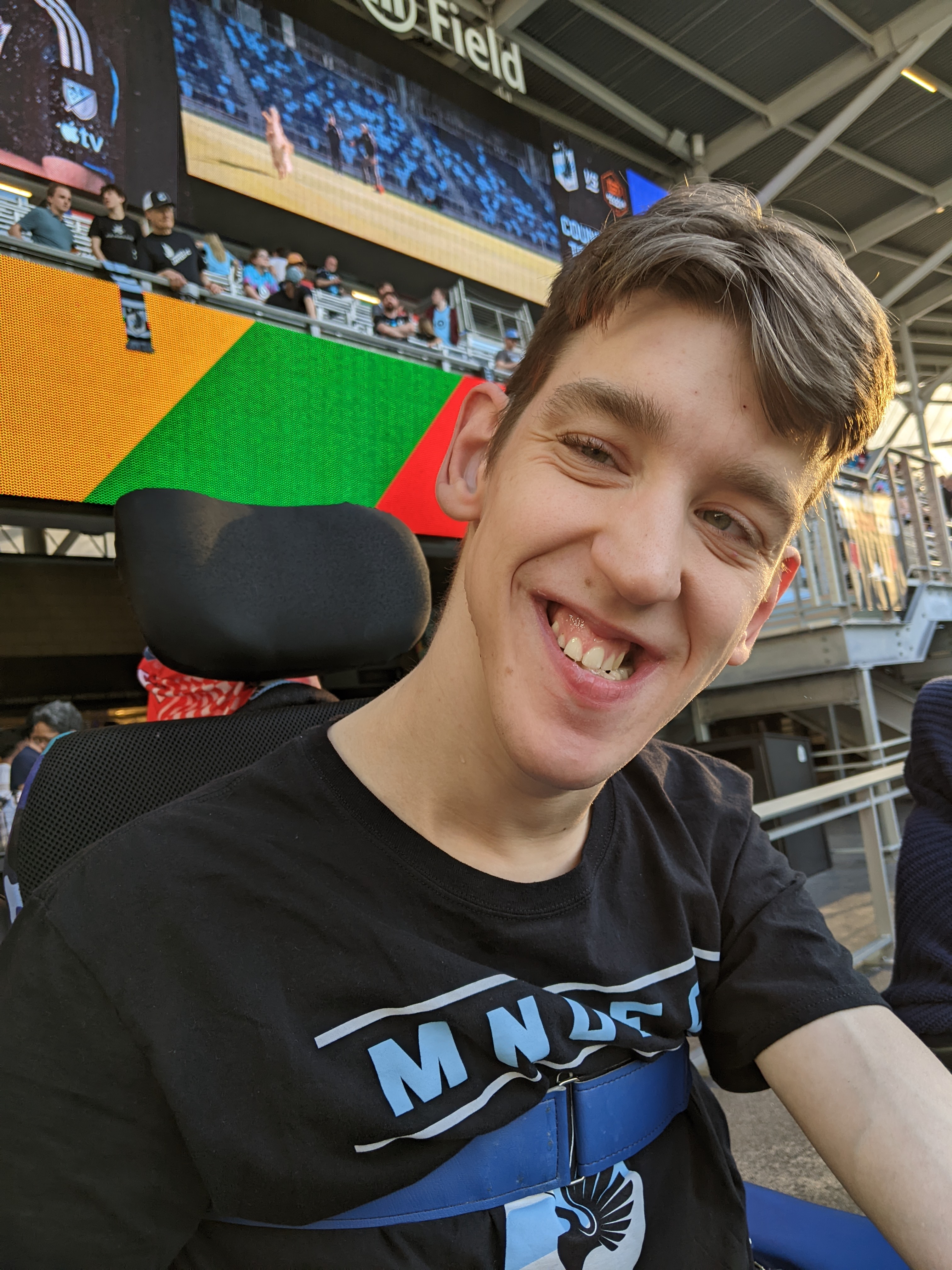 Justin in wheelchair, smiling, wearing MN UFC shirt, in stadium